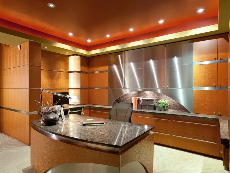 Study with figured wood cabinetry, stainless panels, a curved stone-topped desk and a red ceiling cove