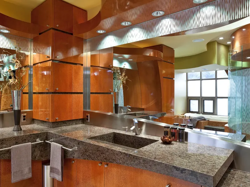 Bath vanity with an integral stone sink, figured wood cabinets and a mirror reflecting the tub