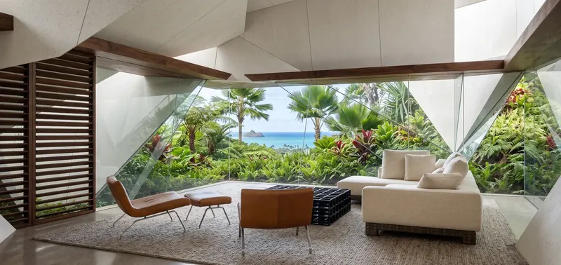 Living room with sloped faceted ceiling, slatted wood screen and angled glass framing jungle and ocean views