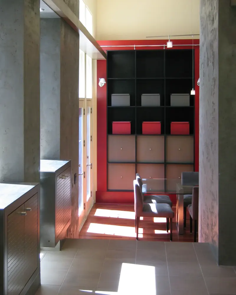 Walkway between plaster columns toward the red and black shelving wall