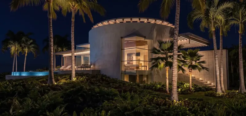 The Inland Oasis rotunda at night, its roofline trellis lit and palms uplit beside a glowing blue pool