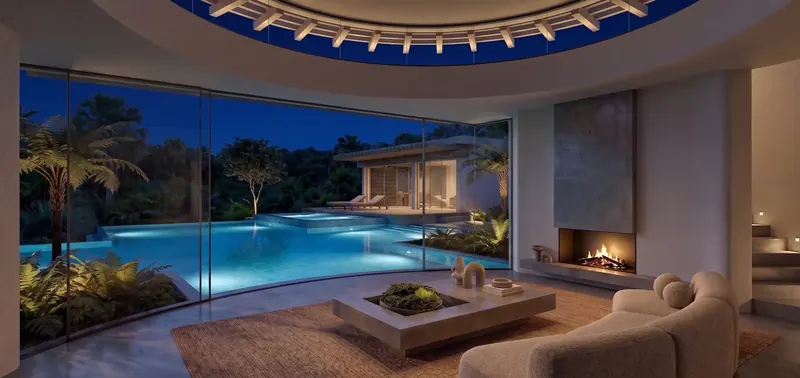 Living room at night with a lit fire, illuminated trellis overhead and glowing blue pools beyond the glass