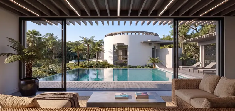 View from a beamed sitting room through wide sliding doors across a pool and wood deck to a white rotunda among palms