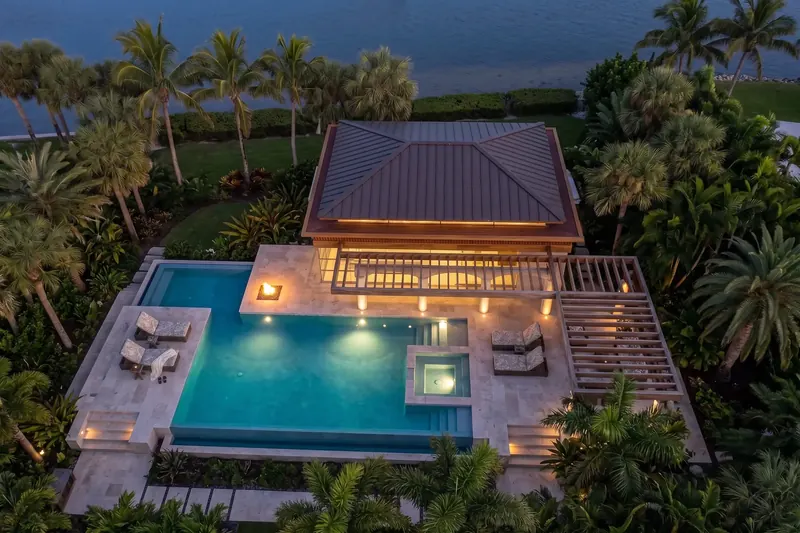 Overhead view of the hipped metal roof, pergola, fire feature and pool, with lawn and water beyond