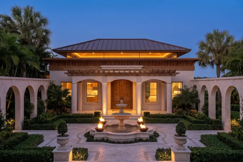 Symmetrical entry court of the home with a tiered stone fountain, fire bowls, arcaded walls and carved wood doors