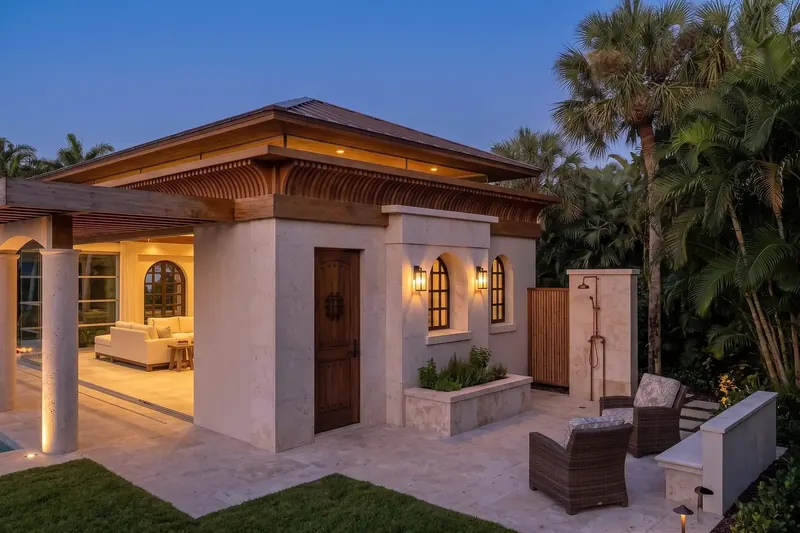 Stone wall with a plank wood door, lanterns, arched windows and an outdoor shower beside wicker chairs