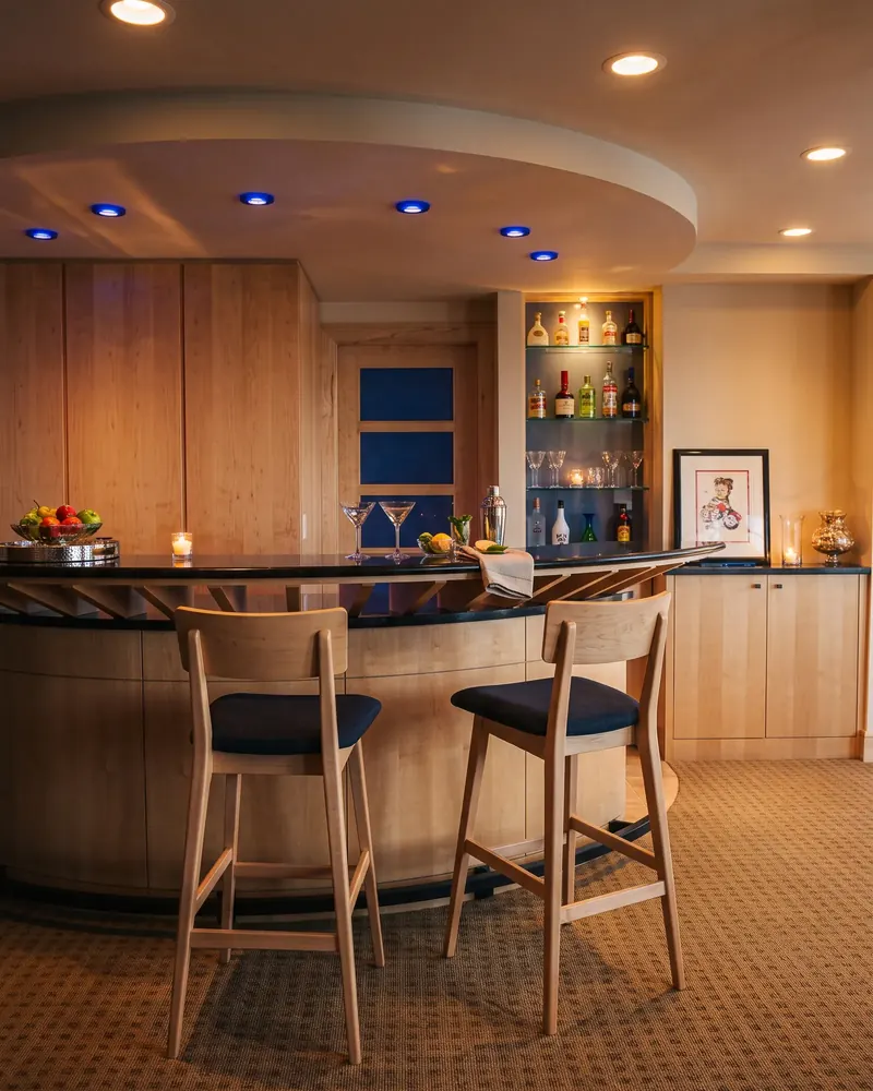 Curved home bar with wood stools beneath a recessed ceiling with accent lights