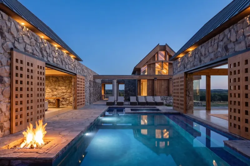 Courtyard pool lit at dusk, a fire pit burning on the stone patio between pavilions with gridded wooden screens