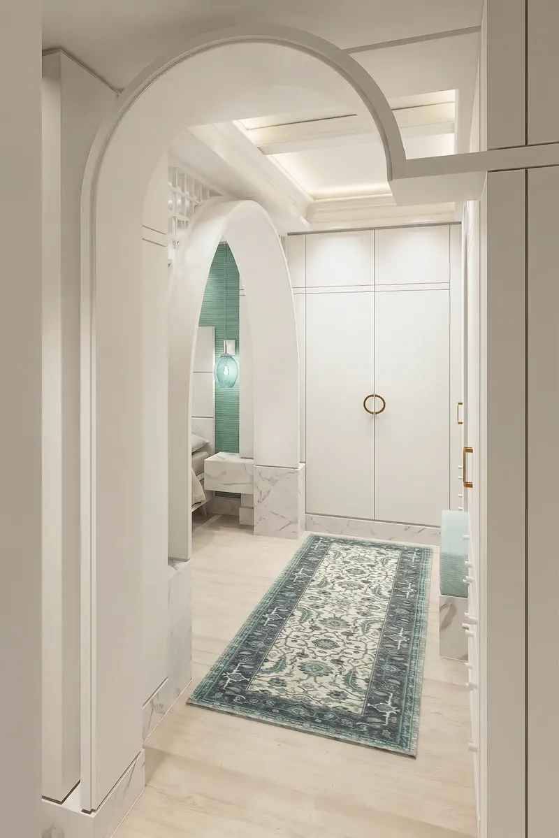 Dressing antechamber with white cabinetry, ring pulls and a teal runner, looking through layered arches to a bed