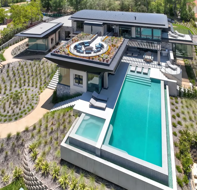 Aerial view of the house, its rooftop terrace and the long infinity-edge pool on a planted hillside