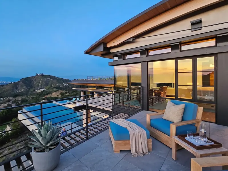 Bedroom deck in late-day light with wood chairs, overlooking the pool and the hills beyond