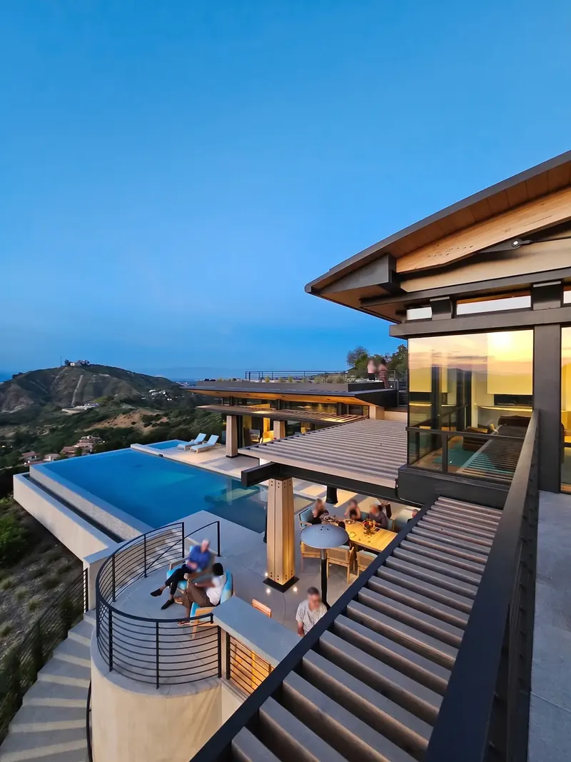 View down from an upper deck to the pool, a circular terrace and the valley at dusk