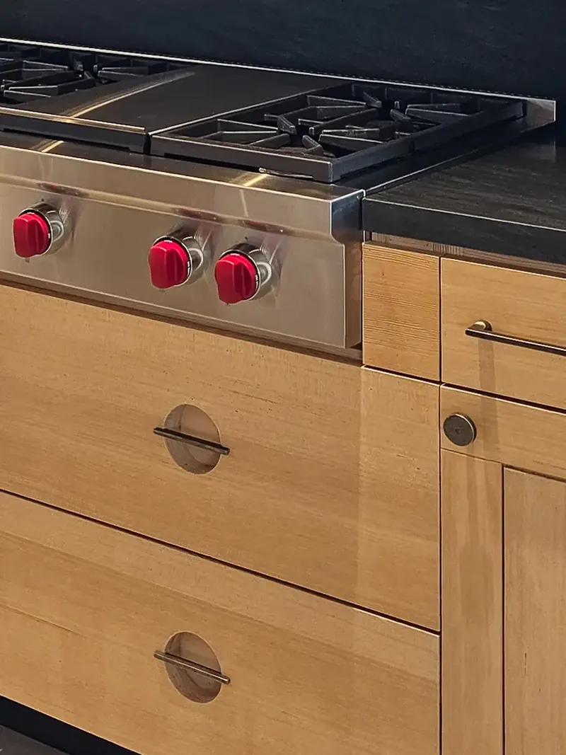 Close detail of fir drawers with round recessed bar pulls beside a professional cooktop