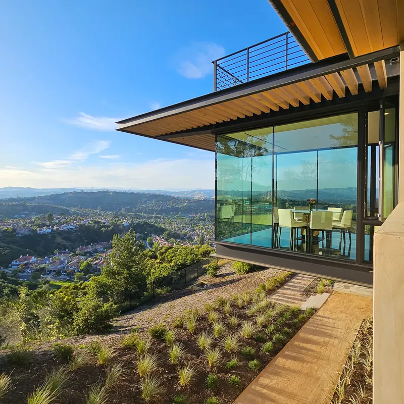 Glass dining room cantilevered over the hillside, its table and chairs suspended above the valley view