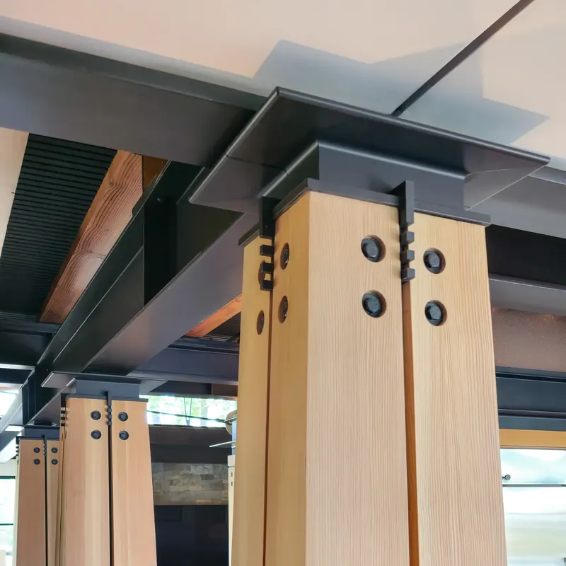 Column capital of bolted timber and dark steel plates meeting a steel beam