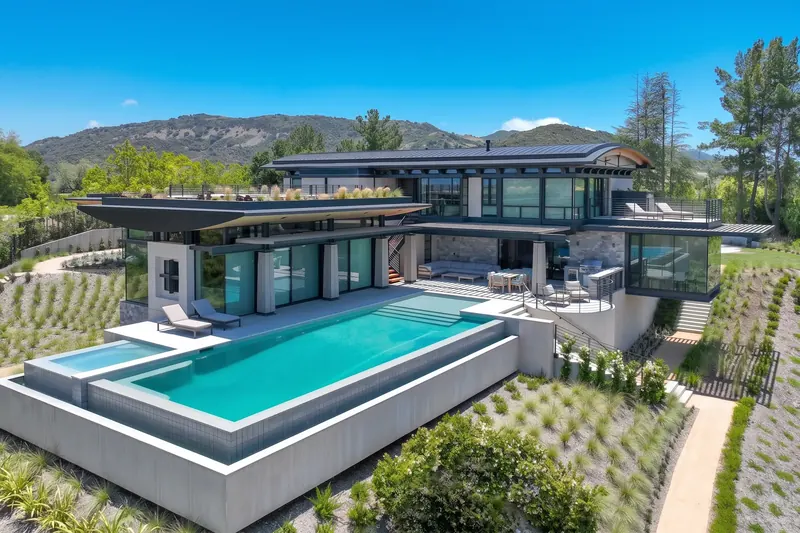 Aerial view of the infinity pool, covered terraces and planted roof, with green mountains beyond