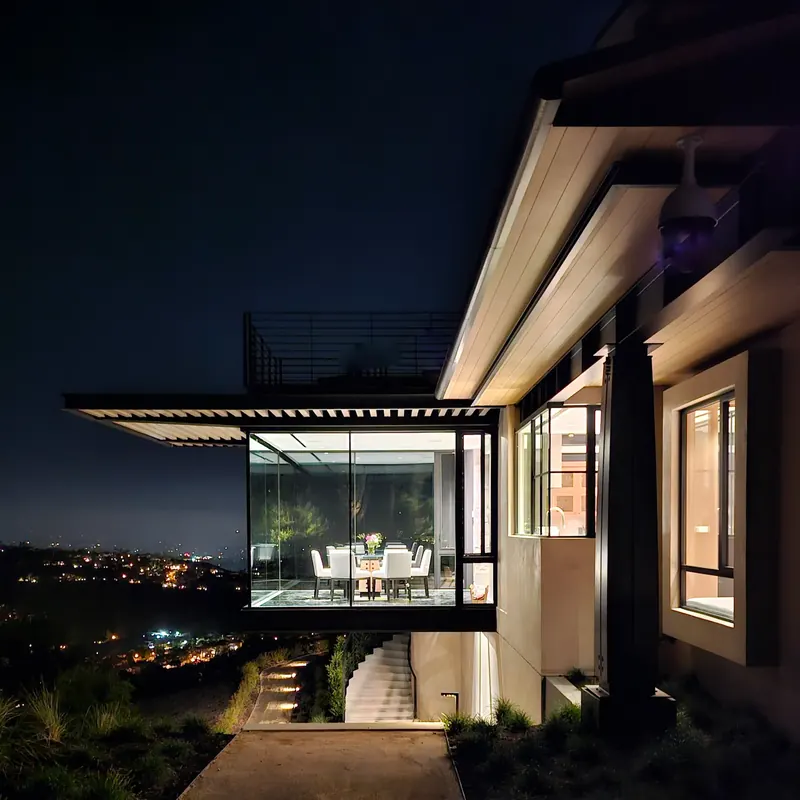 The illuminated glass dining room floating over the hillside at night above the city lights