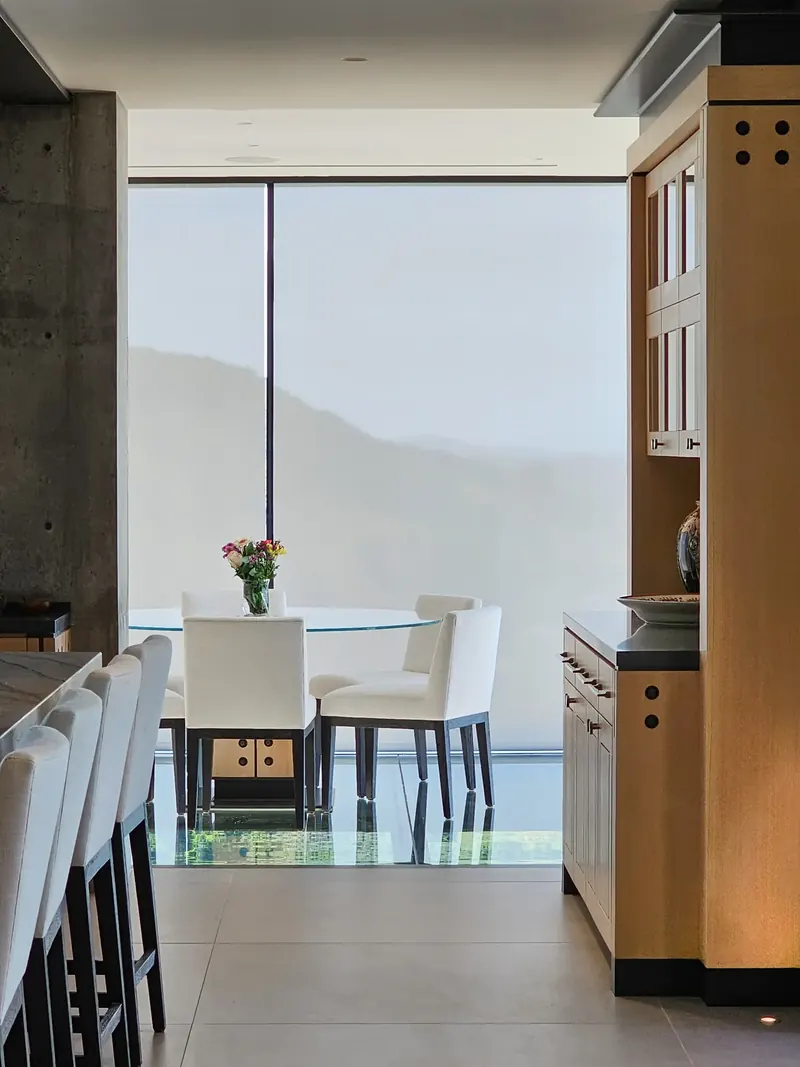 Shades drawn in the glass dining room, softening the hills behind a round table set with flowers