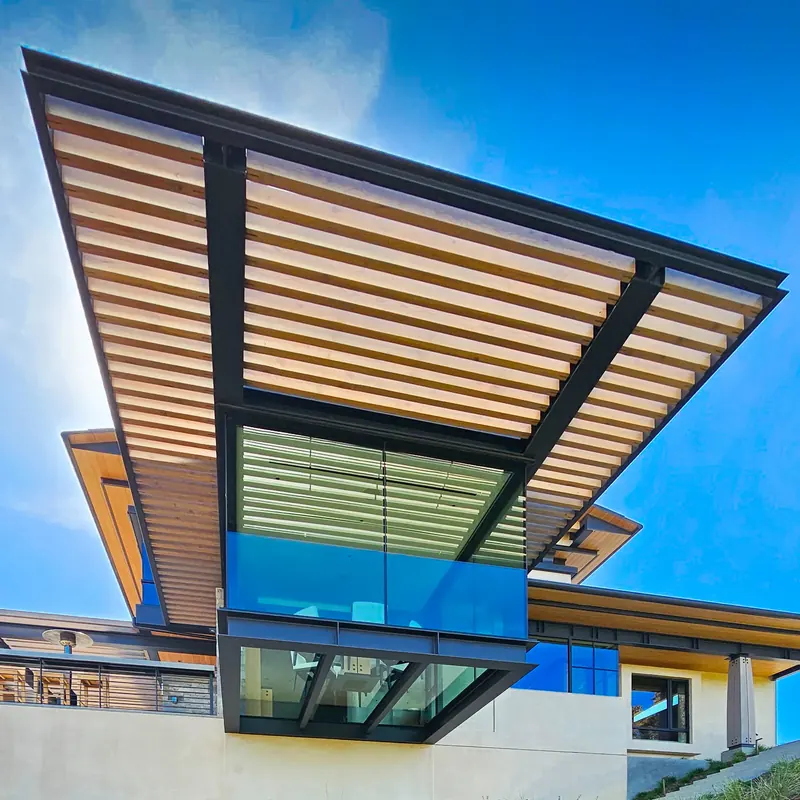 Looking up at the glass dining room's steel frame and the slatted timber sunscreen projecting above it