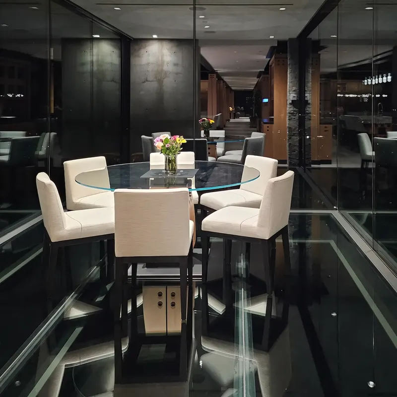 The glass dining room at night, its floor reflecting the table and the long view back through the house