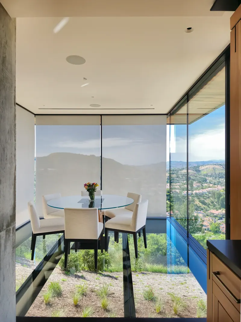 Glass dining room seen from the kitchen, shades lowered on one side and the valley open on the other