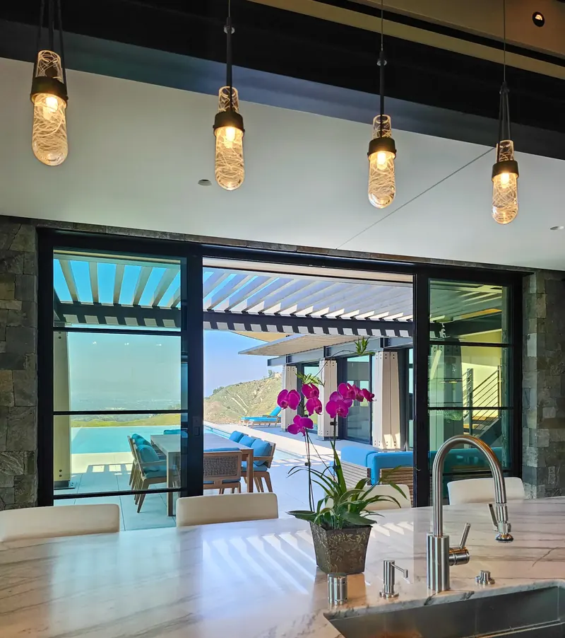 From the kitchen island, glass doors open to the shaded terrace, infinity pool and hills