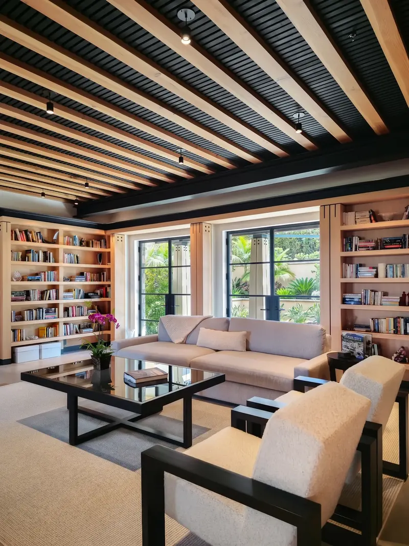 Library with built-in bookshelves, a sofa and armchairs beneath dark and timber ceiling beams