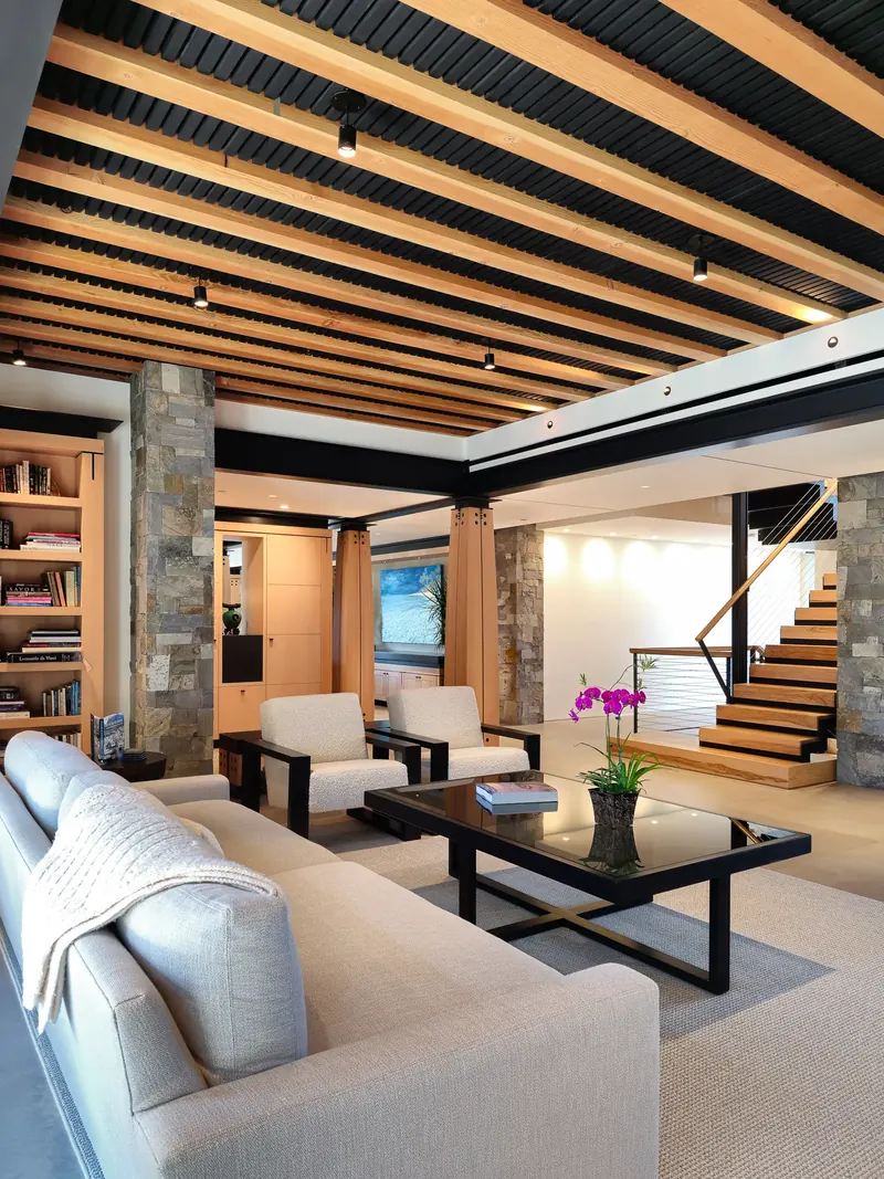 Sitting area beneath timber beams beside stone piers, bookshelves and an open-riser stair