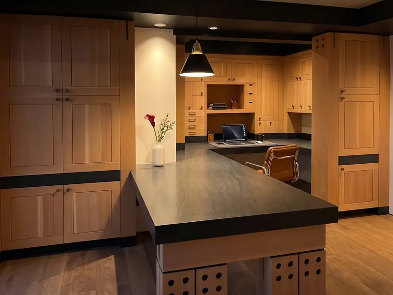 Built-in office in warm wood cabinetry with a dark stone desk and a single pendant light