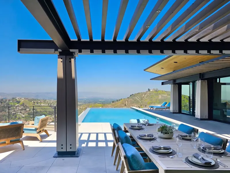 Outdoor dining under a steel and timber trellis beside the infinity pool, hills beyond