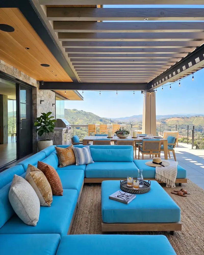 Covered outdoor lounge with a turquoise sectional, dining table and grill overlooking the hills