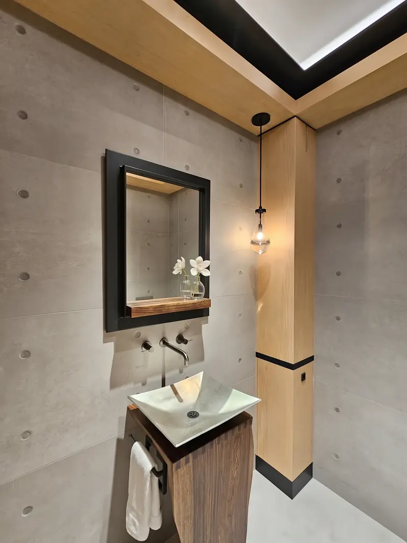Powder room with a white vessel sink on a sculpted wood pedestal against concrete walls