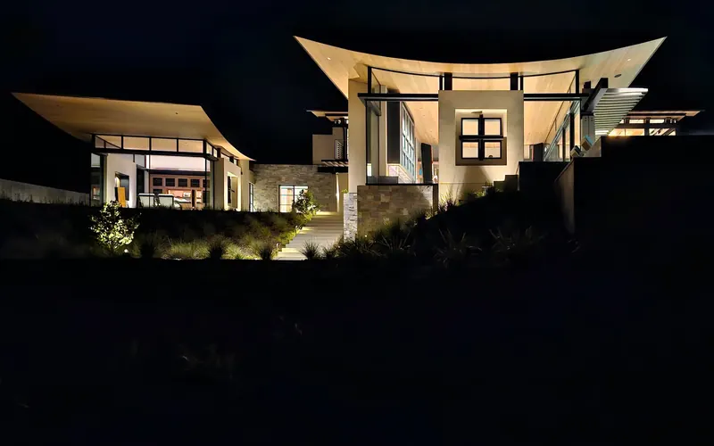 The house glowing at night above a dark hillside