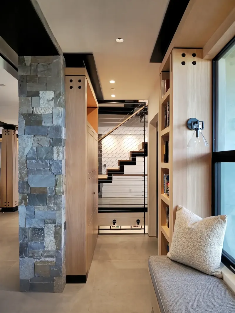Stone pier and wood cabinetry framing a view of the zigzag steel stair, a window seat in the foreground
