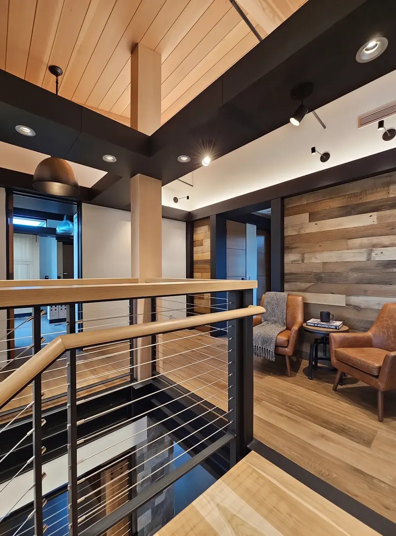 Upper landing with leather chairs against a weathered wood-plank wall, beside the cable-rail stair