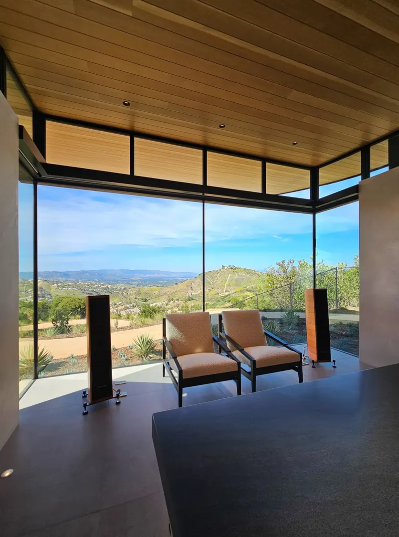 Two lounge chairs and tall speakers face a glass corner and the valley from the study