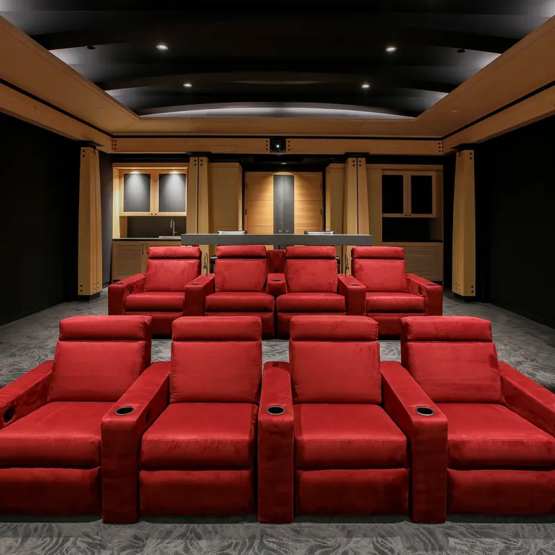 Two rows of red theater recliners before counter seating and wood cabinetry with a wet bar