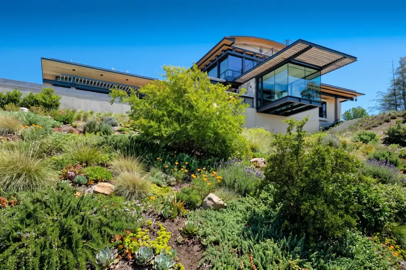 The house seen from the planted hillside below, a glass room projecting out beneath a slatted sunscreen