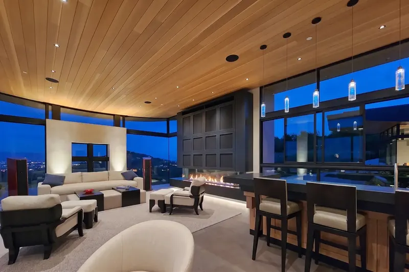 View Room with a linear fireplace, bar seating and windows on all sides at blue hour