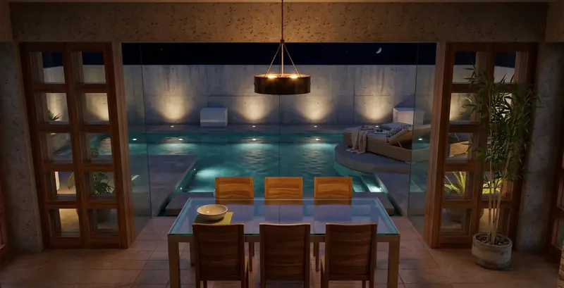Dining room at night looking through glass walls to a lit pool, sun lounge and concrete garden wall