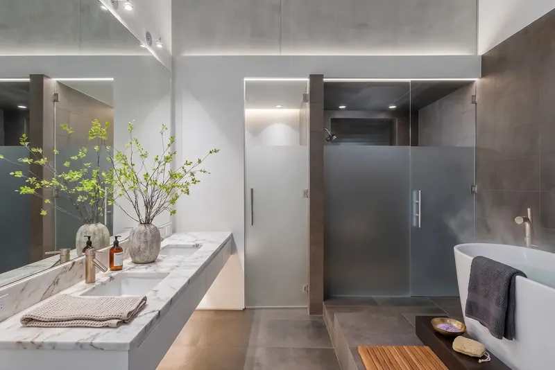 Primary bath with floating marble double vanity, frosted glass shower doors, dark tile and a freestanding tub