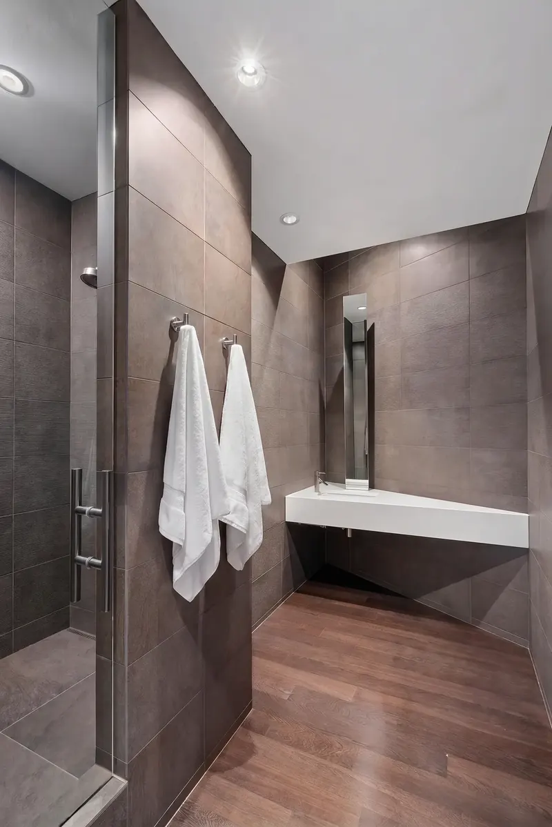Guest bath with angled white floating sink, slender vertical mirror, dark tile walls and wood floor