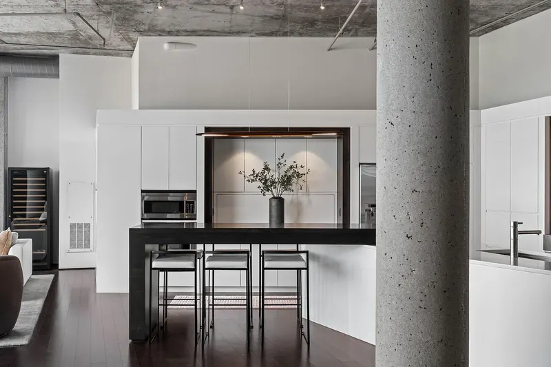 Dark wood bar counter with three stools before handle-free white cabinetry, a concrete column in front
