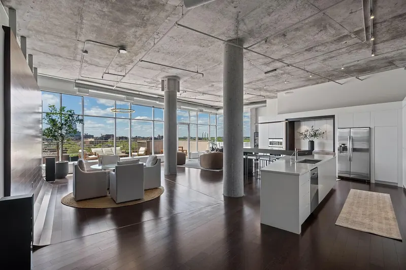 Open daytime living and kitchen space with exposed concrete ceiling, round concrete columns and a wall of windows