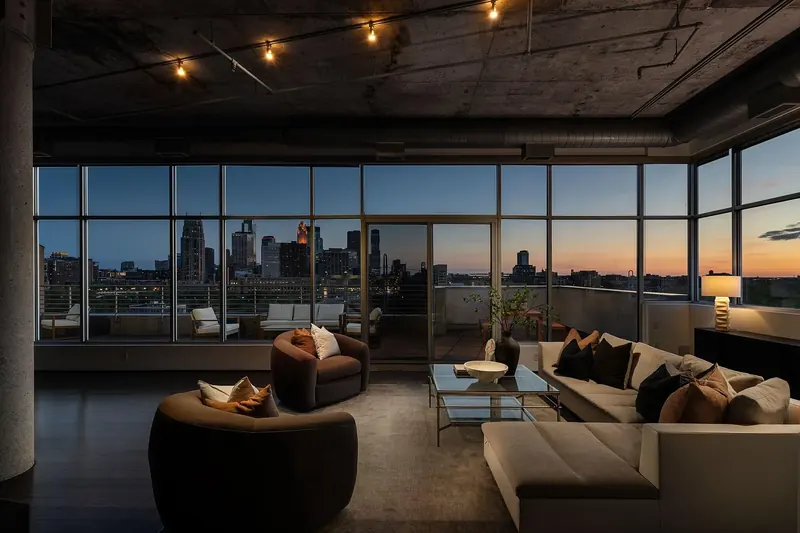 Riverfront Minimalist Penthouse living room at dusk, floor-to-ceiling windows framing the lit Minneapolis skyline