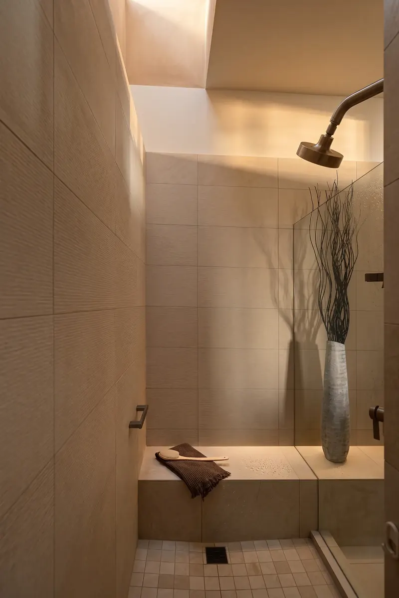 Warm beige tiled shower with a built-in bench, tall vase of branches and light falling from above