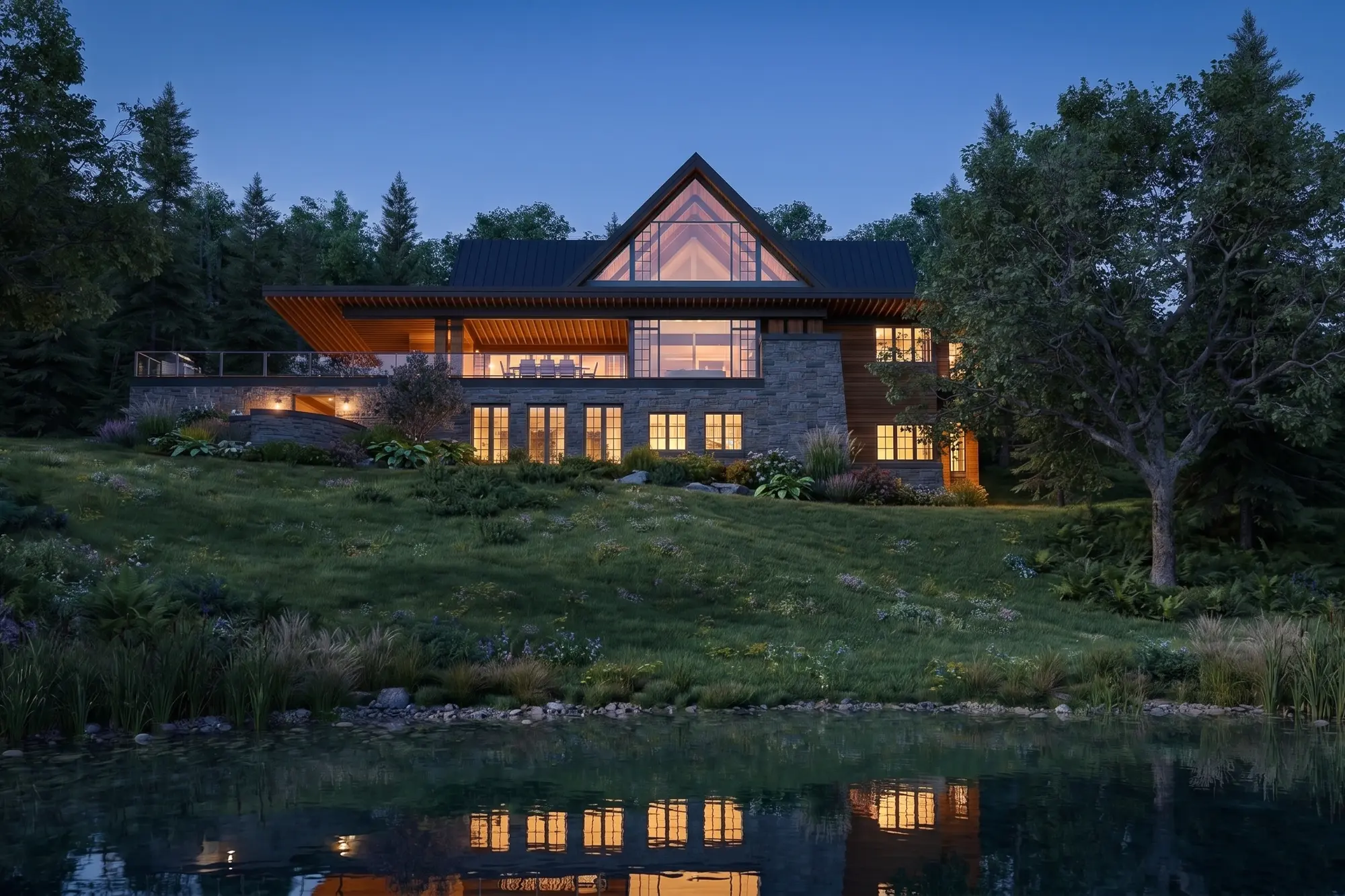 The home at nightfall seen across the water, warm light glowing through the gable and lower-level windows