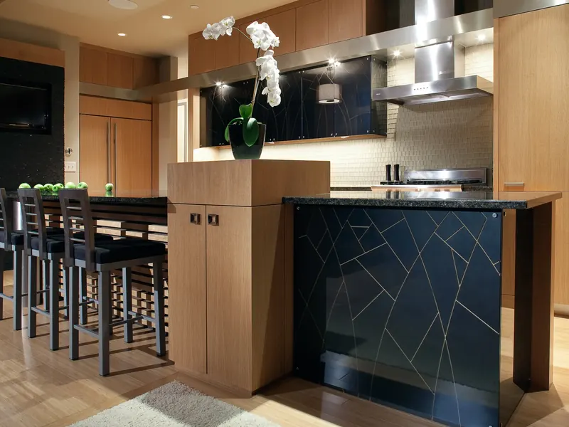 Black island panel inlaid with stylized branch lines beside warm wood cabinetry
