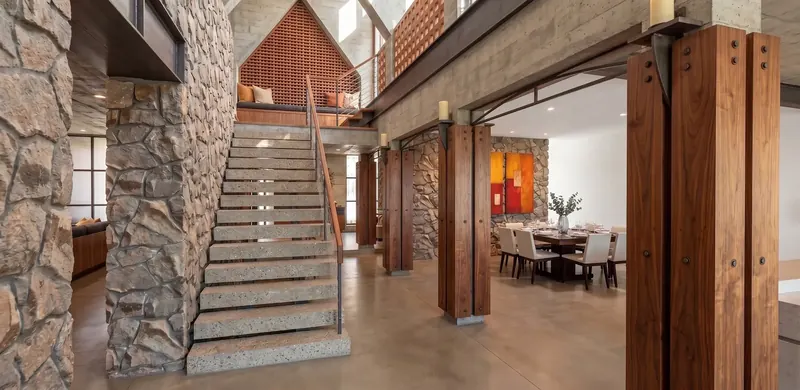 Stone-walled stair rising to a window seat beneath a wooden lattice gable, beside wooden columns with candle holders