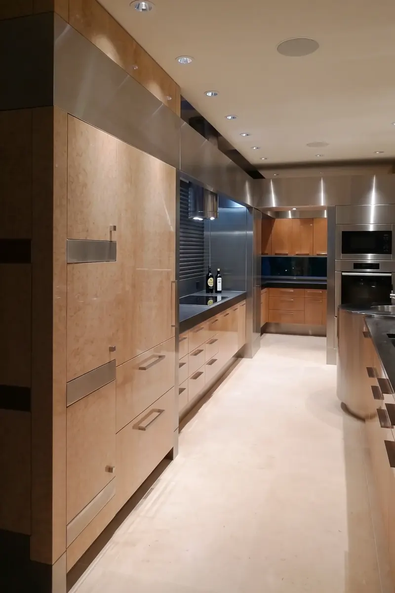Galley of birdseye maple cabinets with stainless pulls, a cooktop under the tubular hood and wall ovens beyond